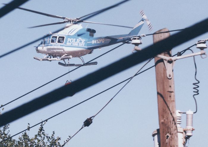 NYPD helicopter with monsoon bucket among telegraph wires